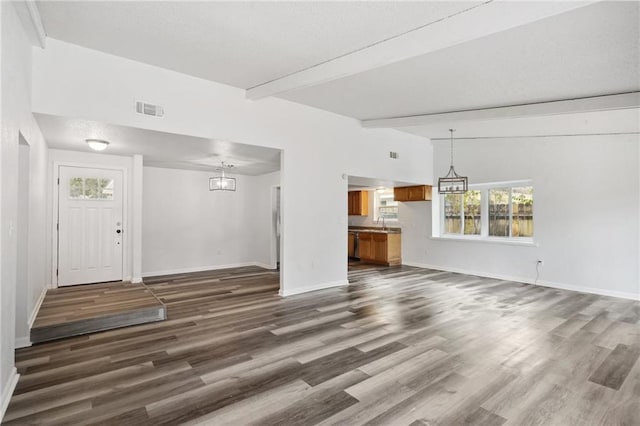 unfurnished living room with a notable chandelier, dark hardwood / wood-style flooring, beam ceiling, and sink