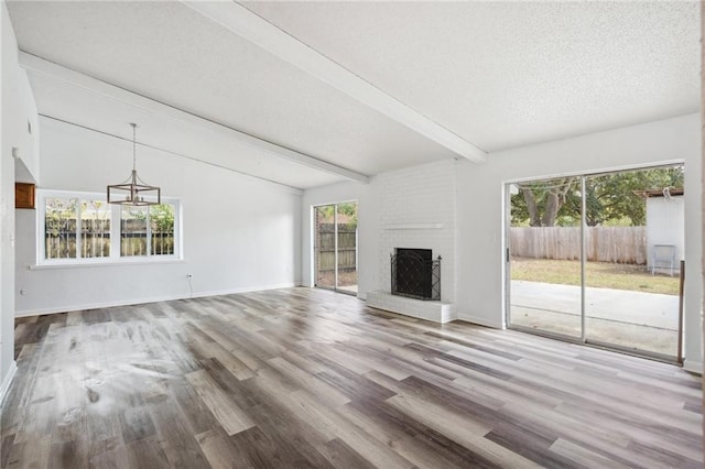 unfurnished living room with a textured ceiling, a brick fireplace, hardwood / wood-style floors, and vaulted ceiling with beams