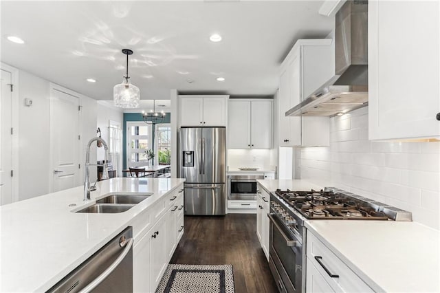 kitchen with white cabinetry, appliances with stainless steel finishes, decorative light fixtures, wall chimney exhaust hood, and sink