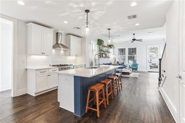 kitchen with a center island with sink, pendant lighting, sink, white cabinets, and wall chimney exhaust hood