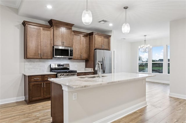 kitchen with a center island with sink, appliances with stainless steel finishes, light stone countertops, pendant lighting, and sink