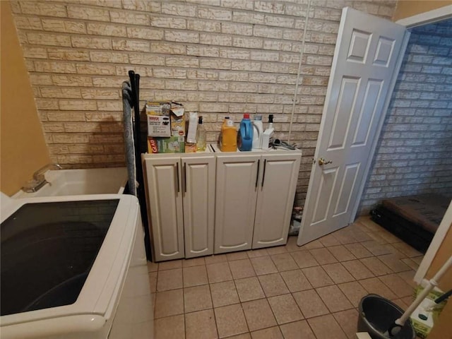 laundry area with brick wall, light tile patterned floors, and washer / clothes dryer