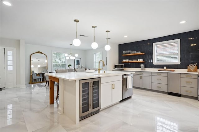 kitchen featuring an island with sink, stainless steel appliances, wine cooler, pendant lighting, and sink