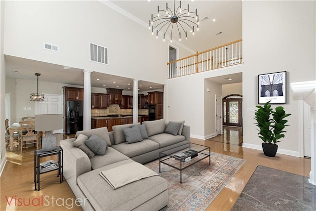 living room featuring a high ceiling, light hardwood / wood-style flooring, crown molding, and a chandelier