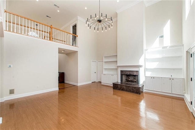 unfurnished living room with a premium fireplace, a chandelier, light hardwood / wood-style flooring, and a high ceiling