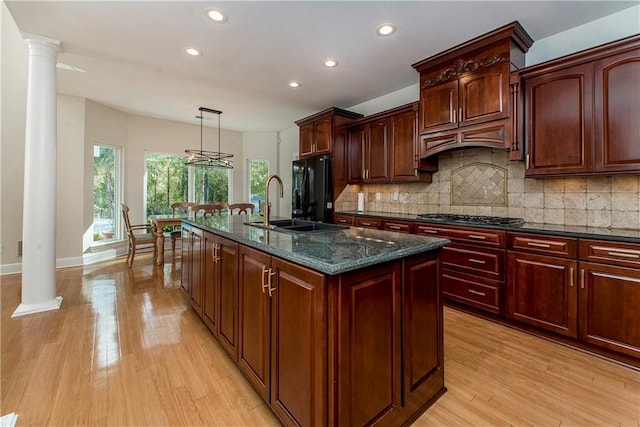 kitchen featuring black refrigerator, dark stone counters, an inviting chandelier, hanging light fixtures, and a kitchen island with sink