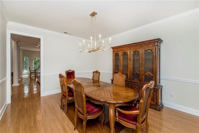 dining room featuring decorative columns, light hardwood / wood-style flooring, crown molding, and a chandelier