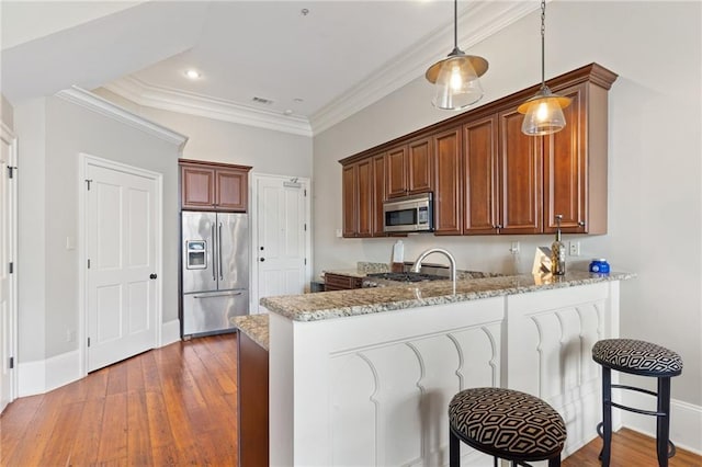 kitchen with stainless steel appliances, dark hardwood / wood-style floors, light stone counters, decorative light fixtures, and kitchen peninsula