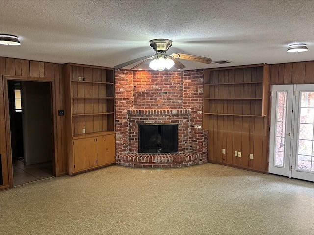 unfurnished living room with a textured ceiling, built in shelves, a fireplace, wooden walls, and ceiling fan