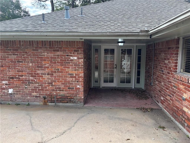 entrance to property with brick siding, a shingled roof, and french doors