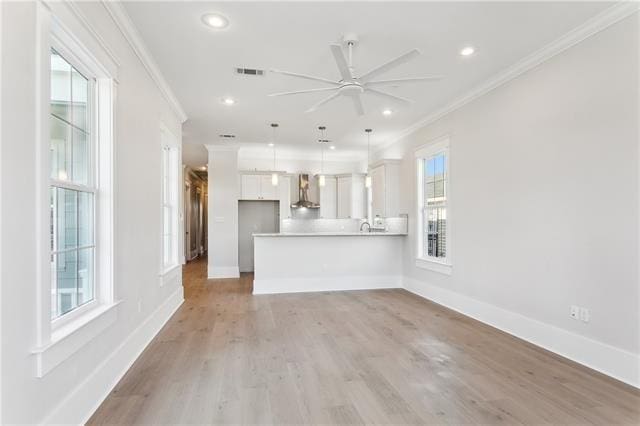 unfurnished living room with light wood-type flooring, ceiling fan, ornamental molding, and plenty of natural light