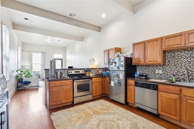 kitchen featuring kitchen peninsula, stainless steel appliances, sink, dark hardwood / wood-style flooring, and beamed ceiling