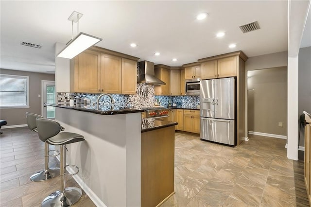 kitchen featuring tasteful backsplash, hanging light fixtures, kitchen peninsula, stainless steel appliances, and wall chimney exhaust hood