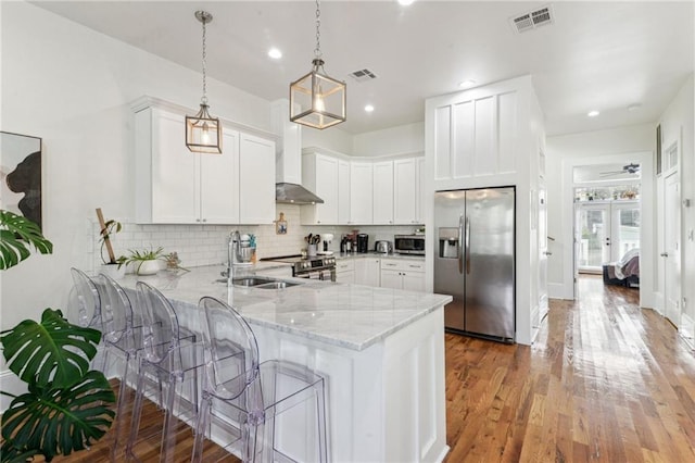 kitchen with kitchen peninsula, appliances with stainless steel finishes, wall chimney exhaust hood, and white cabinetry