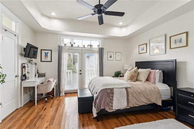 bedroom with ceiling fan, access to exterior, hardwood / wood-style flooring, and a tray ceiling