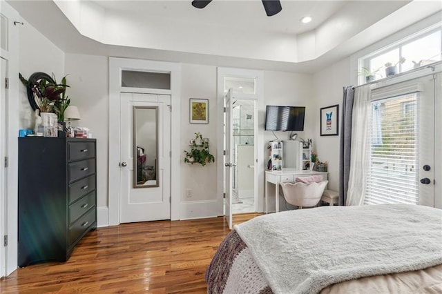 bedroom with ceiling fan, ensuite bath, a raised ceiling, and hardwood / wood-style flooring