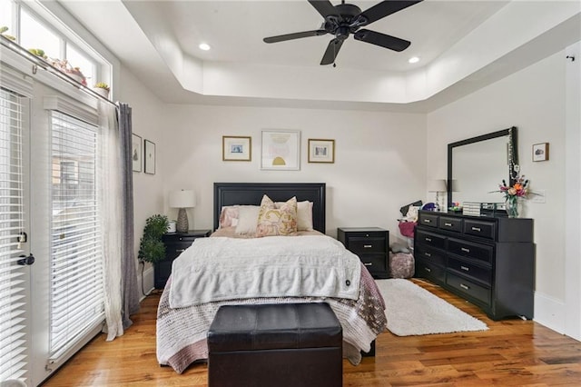 bedroom with ceiling fan, light hardwood / wood-style flooring, and a tray ceiling