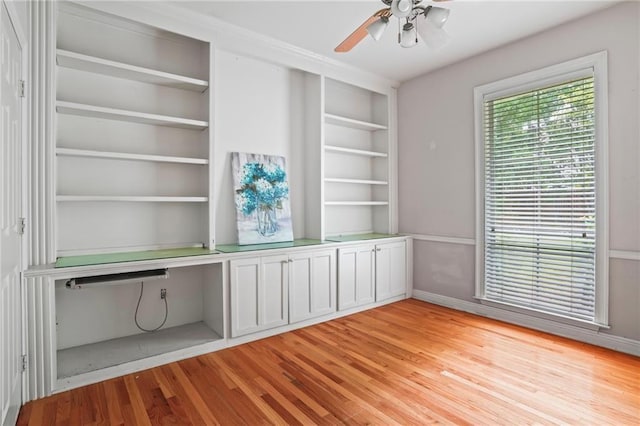 unfurnished office featuring light wood-type flooring, built in desk, ceiling fan, and built in shelves