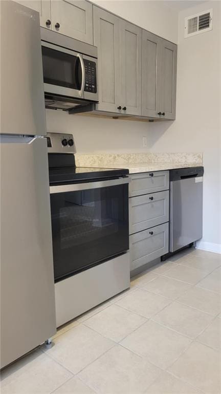 kitchen with gray cabinetry, light tile patterned floors, and appliances with stainless steel finishes