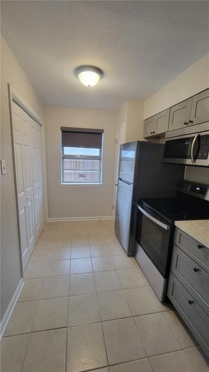 kitchen featuring light stone counters, light tile patterned floors, appliances with stainless steel finishes, and gray cabinetry