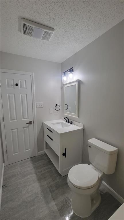 bathroom with a textured ceiling, toilet, and vanity