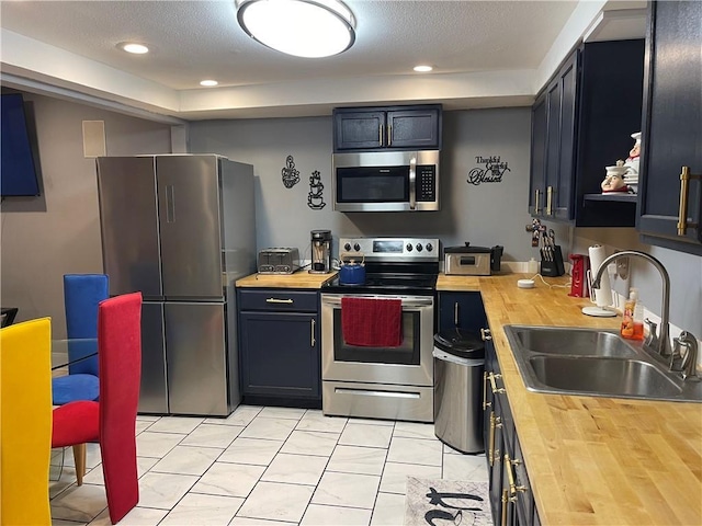 kitchen with light tile patterned flooring, stainless steel appliances, butcher block counters, and sink