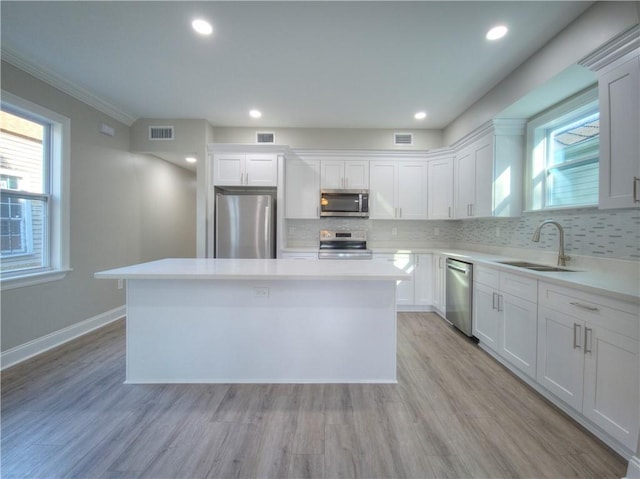 kitchen featuring a center island, white cabinetry, stainless steel appliances, light hardwood / wood-style floors, and sink