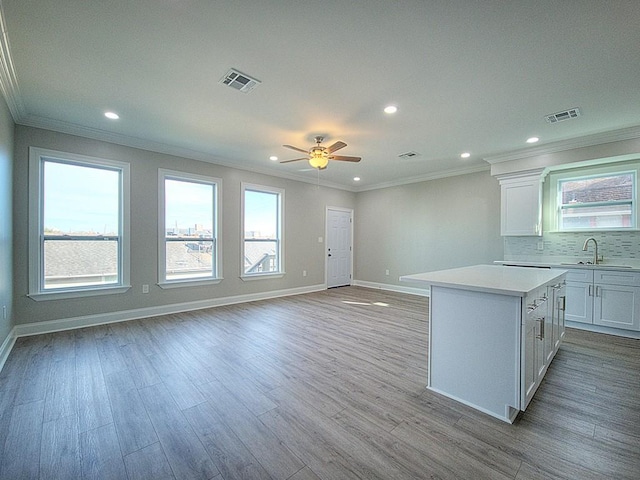 kitchen with a kitchen island, white cabinetry, tasteful backsplash, light hardwood / wood-style flooring, and crown molding