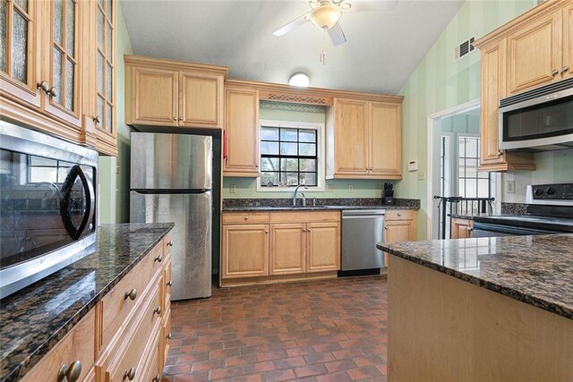 kitchen with sink, lofted ceiling, stainless steel appliances, and dark stone countertops