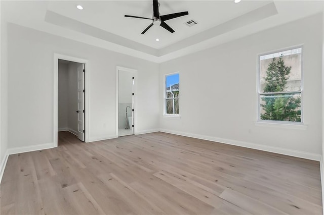 unfurnished bedroom with ceiling fan, ensuite bath, and a raised ceiling