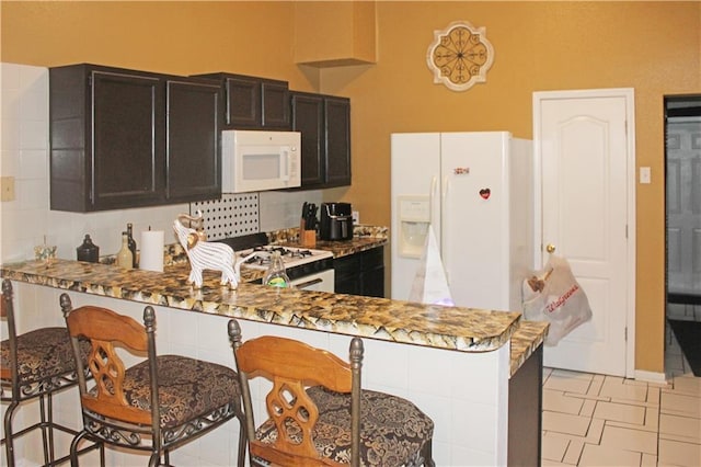 kitchen featuring decorative backsplash, white appliances, kitchen peninsula, and light tile patterned flooring