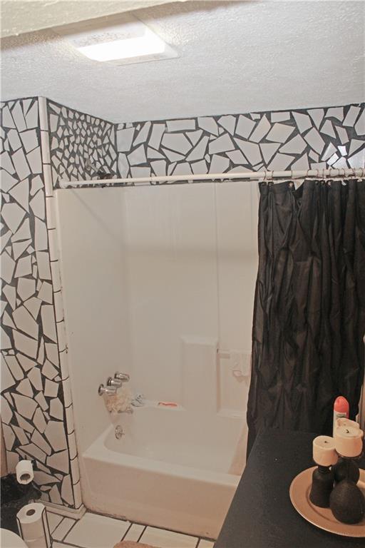 bathroom with a textured ceiling, shower / bathtub combination with curtain, and tile patterned floors