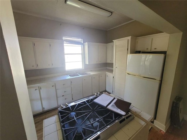 kitchen with hardwood / wood-style flooring, white cabinetry, tile counters, and white fridge