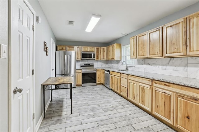 kitchen featuring appliances with stainless steel finishes, backsplash, light brown cabinetry, light stone countertops, and sink