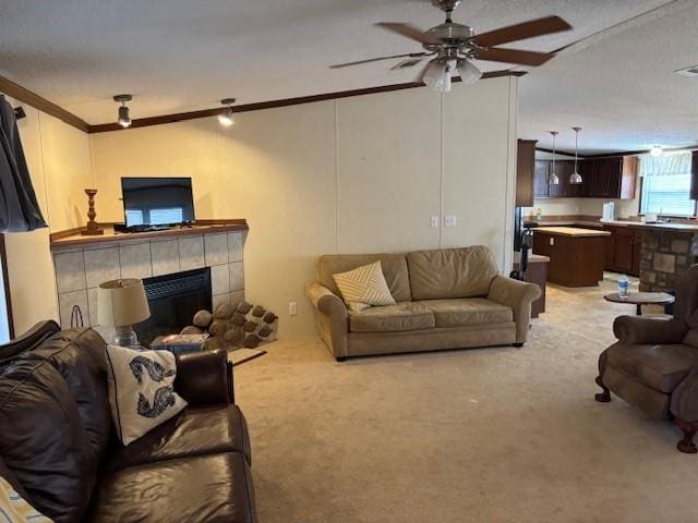 carpeted living room featuring a tiled fireplace, ornamental molding, a textured ceiling, and ceiling fan