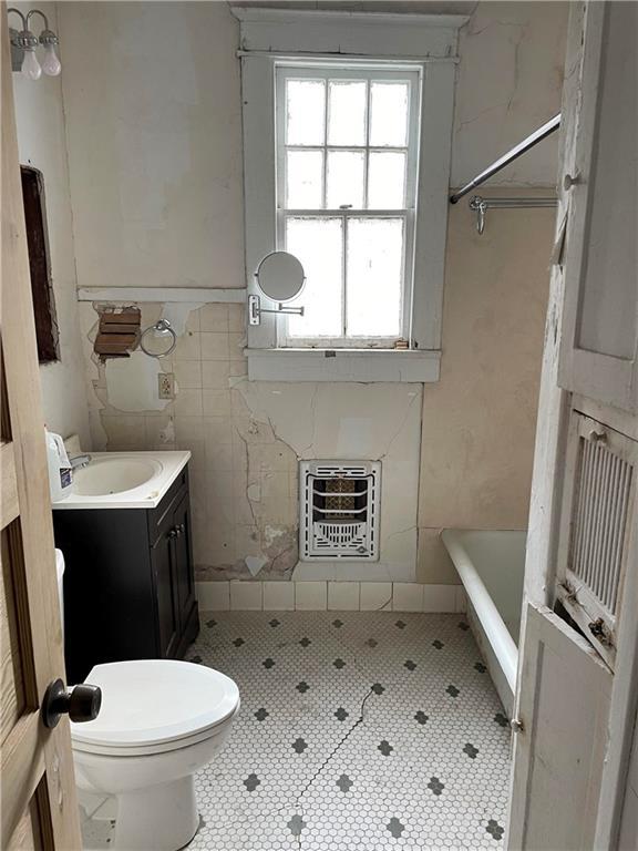 bathroom with toilet, heating unit, tile walls, vanity, and a tub