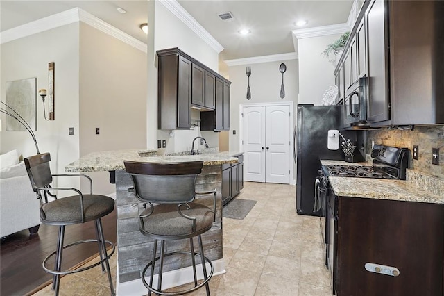 kitchen with ornamental molding, dark brown cabinets, light stone counters, and black appliances