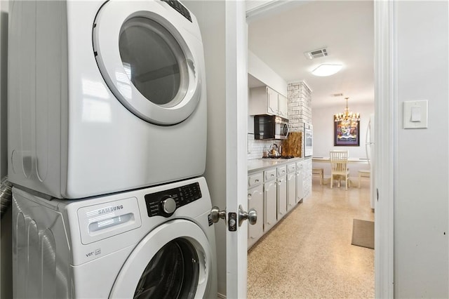 clothes washing area with stacked washer and dryer and a chandelier