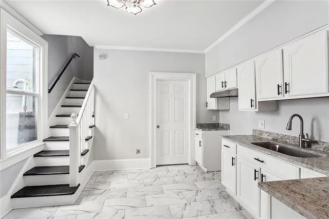 kitchen featuring sink, light stone counters, ornamental molding, and white cabinetry