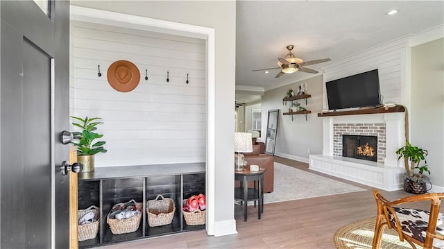 mudroom with light wood-type flooring, ceiling fan, ornamental molding, and a fireplace