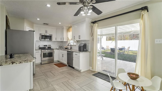 kitchen with light stone countertops, backsplash, white cabinetry, and stainless steel appliances