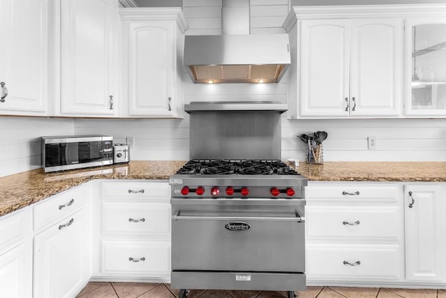 kitchen with dark stone countertops, stainless steel appliances, white cabinets, light tile patterned flooring, and wall chimney exhaust hood