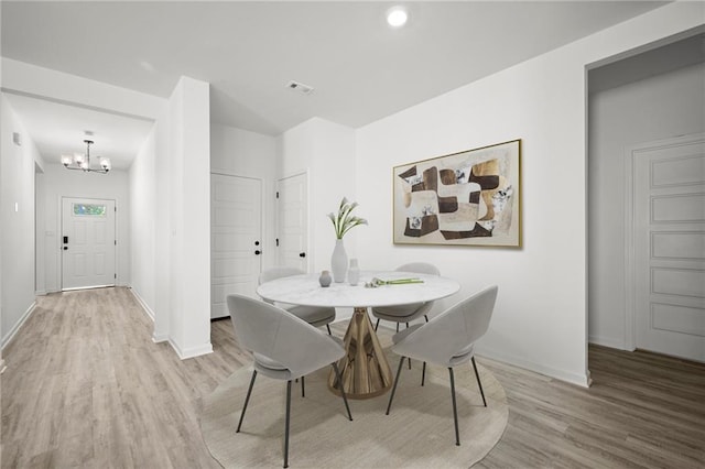 dining space featuring baseboards, visible vents, wood finished floors, and an inviting chandelier