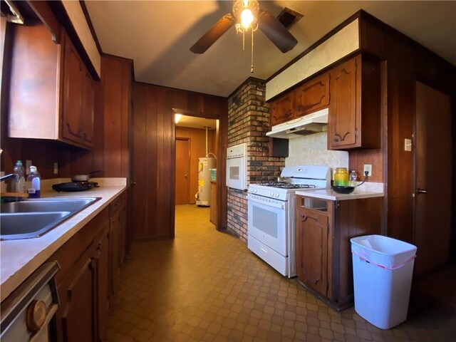 kitchen with sink, white appliances, water heater, ceiling fan, and wooden walls