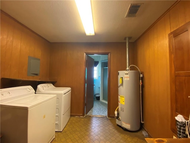 clothes washing area with wood walls, washer and clothes dryer, a textured ceiling, and gas water heater