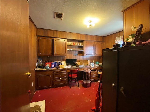 carpeted office featuring built in desk and wood walls