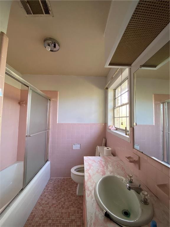 full bathroom featuring bath / shower combo with glass door, tile walls, vanity, toilet, and tile patterned floors