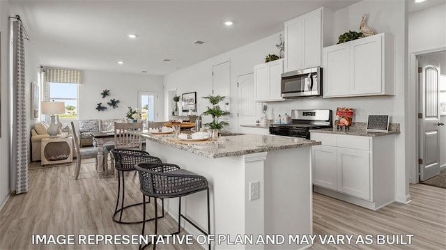 kitchen with an island with sink, white cabinetry, light hardwood / wood-style flooring, and appliances with stainless steel finishes