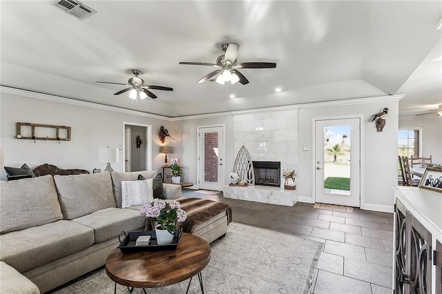 living area with baseboards, visible vents, a fireplace, ornamental molding, and ceiling fan