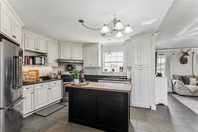 kitchen with under cabinet range hood, butcher block countertops, a chandelier, stainless steel appliances, and a sink